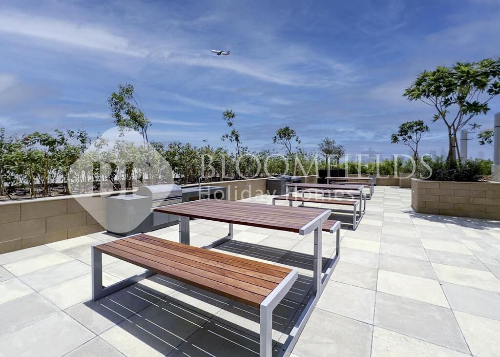 Eine Dachterrasse mit Sitzgelegenheiten im Freien, wolkenloser Himmel und ein Flugzeug in der Ferne.