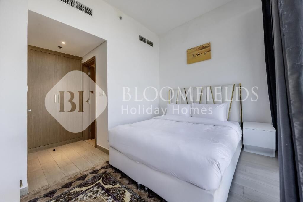 Un dormitorio con una cama grande, una mesita de noche y una lámpara de noche pequeña. Se ve una puerta que da a otra habitación y una obra de arte colgada en la pared.