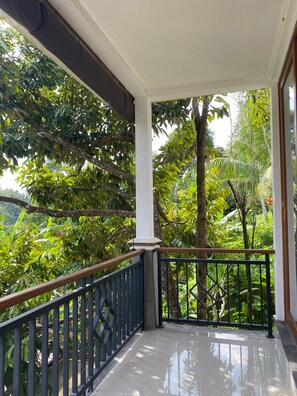 En balkon med udsigt til frodigt grønt og en hvid søjle.