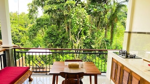 A balcony with a dining table and chairs, a red sofa, and a kitchen area with a gas stove. - Vishnu Villa (Ubud)