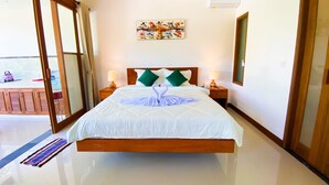 A hotel room with a large bed, two bedside lamps, a painting on the wall, and a sliding glass door leading to an outdoor area. - Vishnu Villa (Ubud)