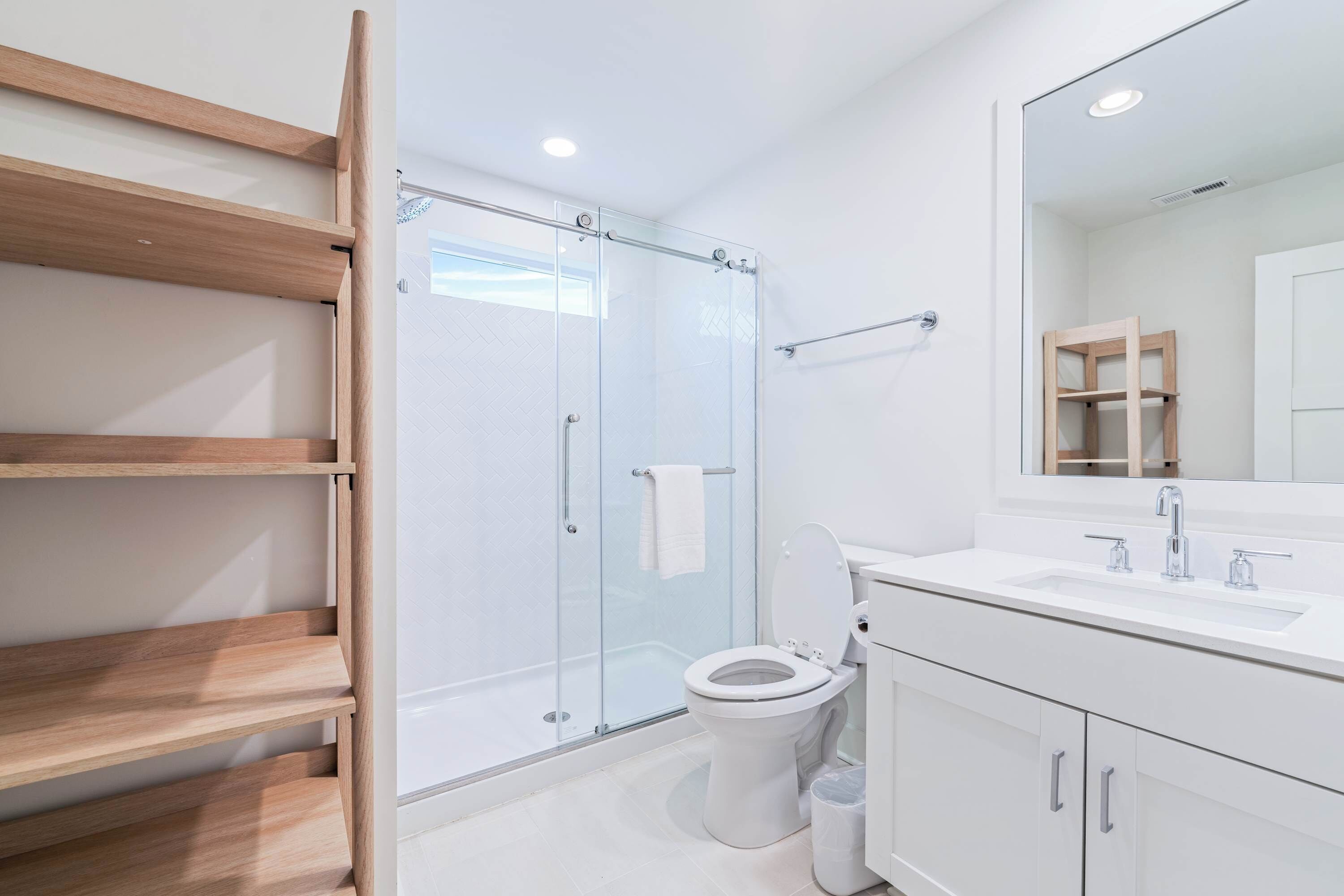 Une salle de bain moderne avec une douche à parois de verre, des toilettes, un lavabo avec un miroir et des étagères en bois.