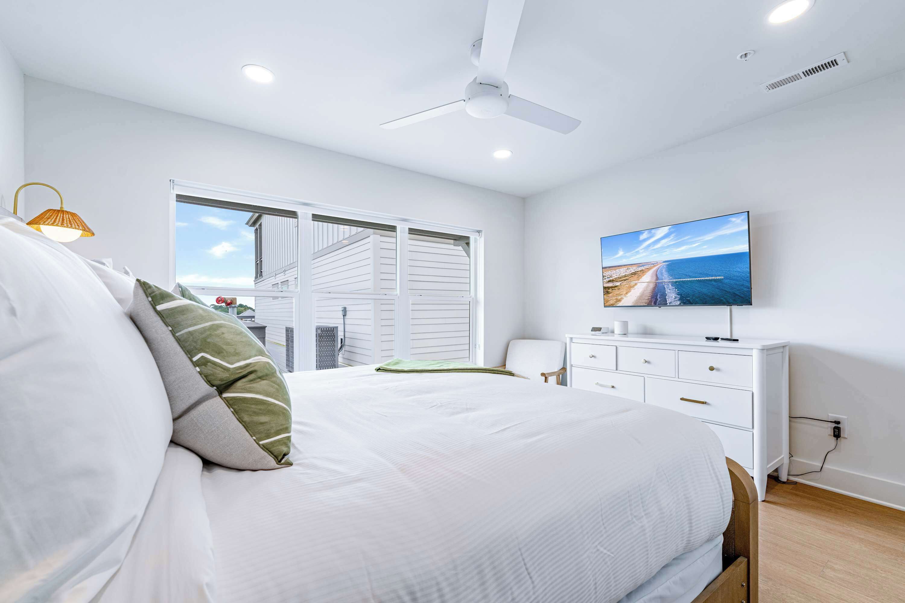 Een slaapkamer met een bed, een televisie, een dressoir en een raam met uitzicht op het strand.