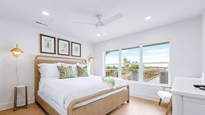 A modern bedroom with a wooden bed, a ceiling fan, and a large window offering a view of the outdoors.