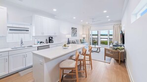 A modern kitchen with white cabinetry, a central island with bar stools, a dining area with a table and chairs, and a large window offering a view. - Waterfront Villa with Pool & Boat Slip (Georgetown)