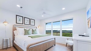 A modern bedroom with a large bed, bedside tables, a desk, and a view of the outdoors. - Waterfront Villa with Pool & Boat Slip (Georgetown)