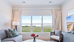 A living room with a sofa, armchair, and a coffee table with a vase of flowers. - Creekside Villa w. Pool + Boat Slip (Georgetown)