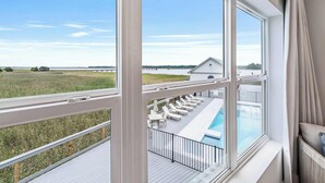 A balcony with a pool, lounge chairs, and a view of a body of water and distant buildings. - Creekside Villa w. Pool + Boat Slip (Georgetown)