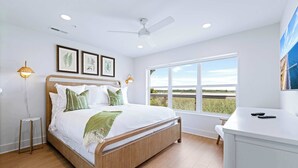 A modern bedroom with a wooden bed, a desk, and a large window offering a view of the outdoors. - Marsh View Cottage with Pool + Boat Slip (Georgetown)