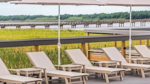 Een zwembadterras met ligbedden en parasols, met in de verte een helder zicht op een brug en een rustig zwembad.