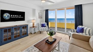 Een moderne woonkamer met een groot raam met uitzicht op de oceaan, een flatscreen televisie aan de muur, een houten salontafel en een gestreepte bank.