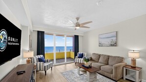 Een moderne woonkamer met een bank, fauteuils, een salontafel en een televisiescherm waarop 'SUNLIT Vacation Rentals' staat.