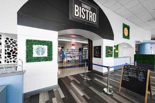 A Sunrise Bistro with a Starbucks logo on the wall, a chalkboard menu, and a blue rope barrier. - Vista Bleu - Ocean Walk (Daytona Beach)