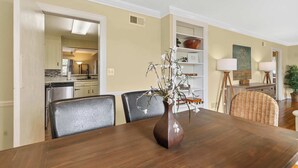 Un coin repas avec une table en bois, des chaises, un vase de fleurs et une cuisine en arrière-plan.