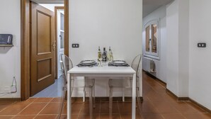 A dining area with a white table, two chairs, and a window. There are wine bottles and glasses on the table.