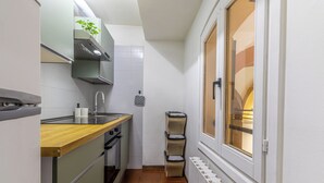 A compact kitchen with a wooden countertop, a built-in oven, a sink, and a window with a view of a building.