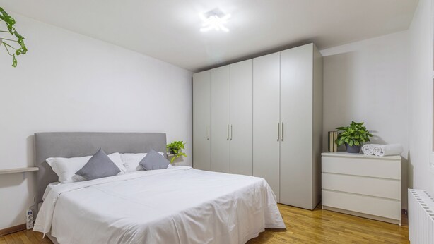 A bedroom with a bed, a wardrobe, a bedside table with a plant, and a radiator.