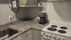 A kitchen with white cabinets, a stainless steel sink, a microwave, a coffee maker, and a stove.