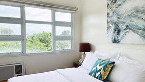A bedroom with a bed, a window, a wall-mounted lamp, and a painting. - Cozy 2BR Condo at Seawind Davao • Smart Lock • Netflix 4K & YouTube Premium (Davao City)