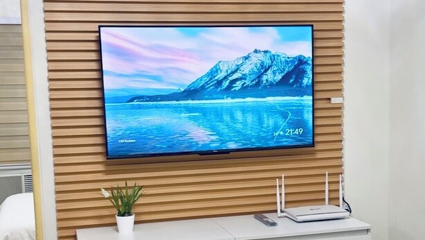 A modern room with a wooden slat wall, a flat-screen TV displaying a scenic image, a white dresser, and a table with a vase of flowers. - Cozy 2BR Condo at Seawind Davao • Smart Lock • Netflix 4K & YouTube Premium (Davao City)