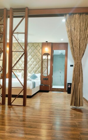 A hotel room with a bed, wooden floor, a mirror, a door, and a curtain. - HOTEL BIVA (Silchar)