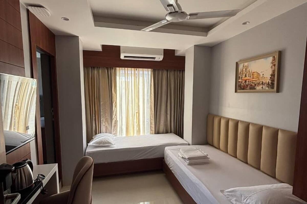A hotel room with a bed, a desk, a chair, a ceiling fan, and a painting on the wall.