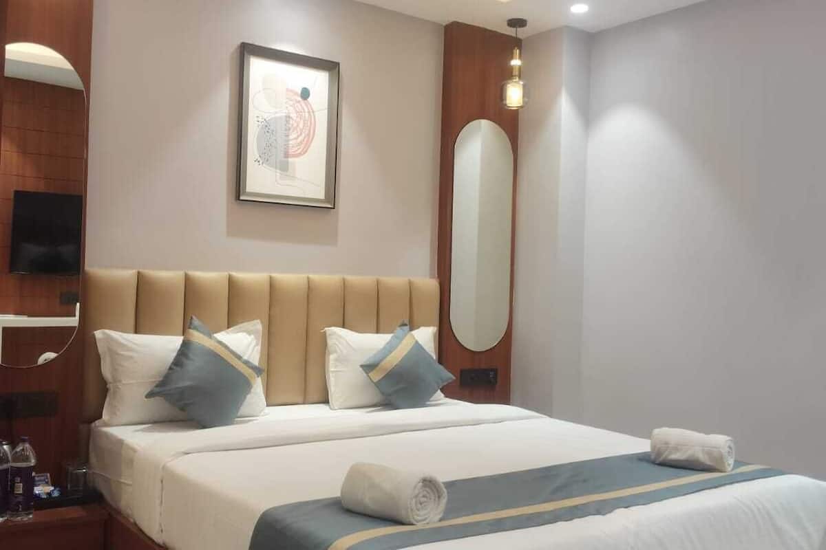 A modern hotel room with a large bed, a ceiling fan, recessed lighting, a wall-mounted TV, and a framed artwork.