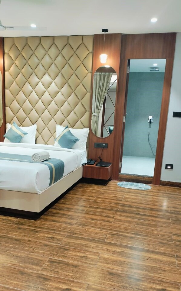 A modern hotel room with a large bed, a bedside table with a lamp, a mirror, and a shower area. - HOTEL BIVA (Silchar)
