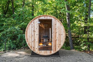 A wooden sauna structure with a bench inside, surrounded by a forest. - Deer Run Lodge/Indoor Pool/Basketball/Hot Tub (Terre Haute)