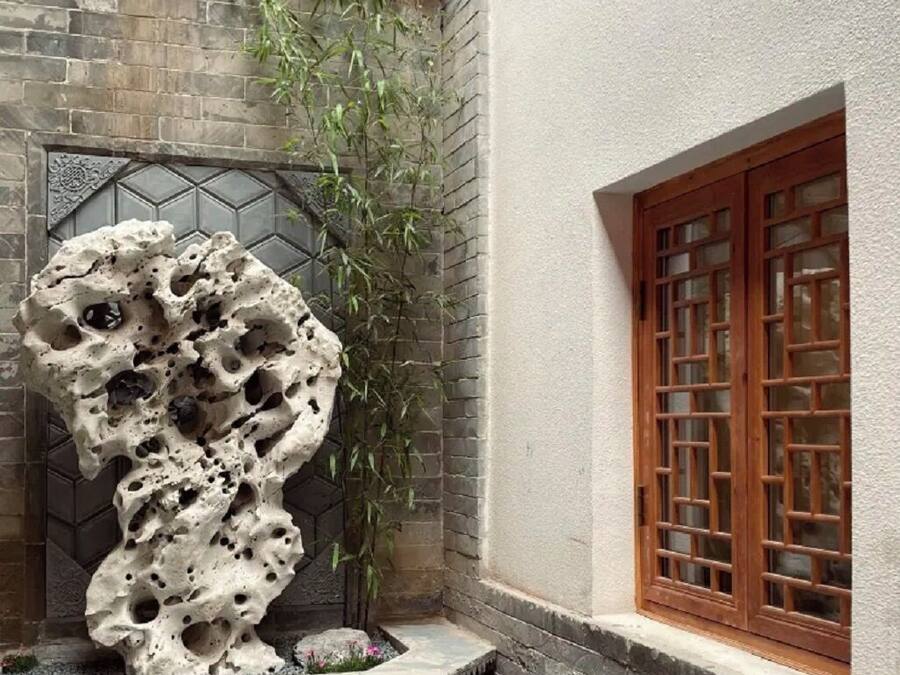 Une cour traditionnelle agrémentée d’une sculpture en pierre, de bambous et d’une fenêtre en bois.