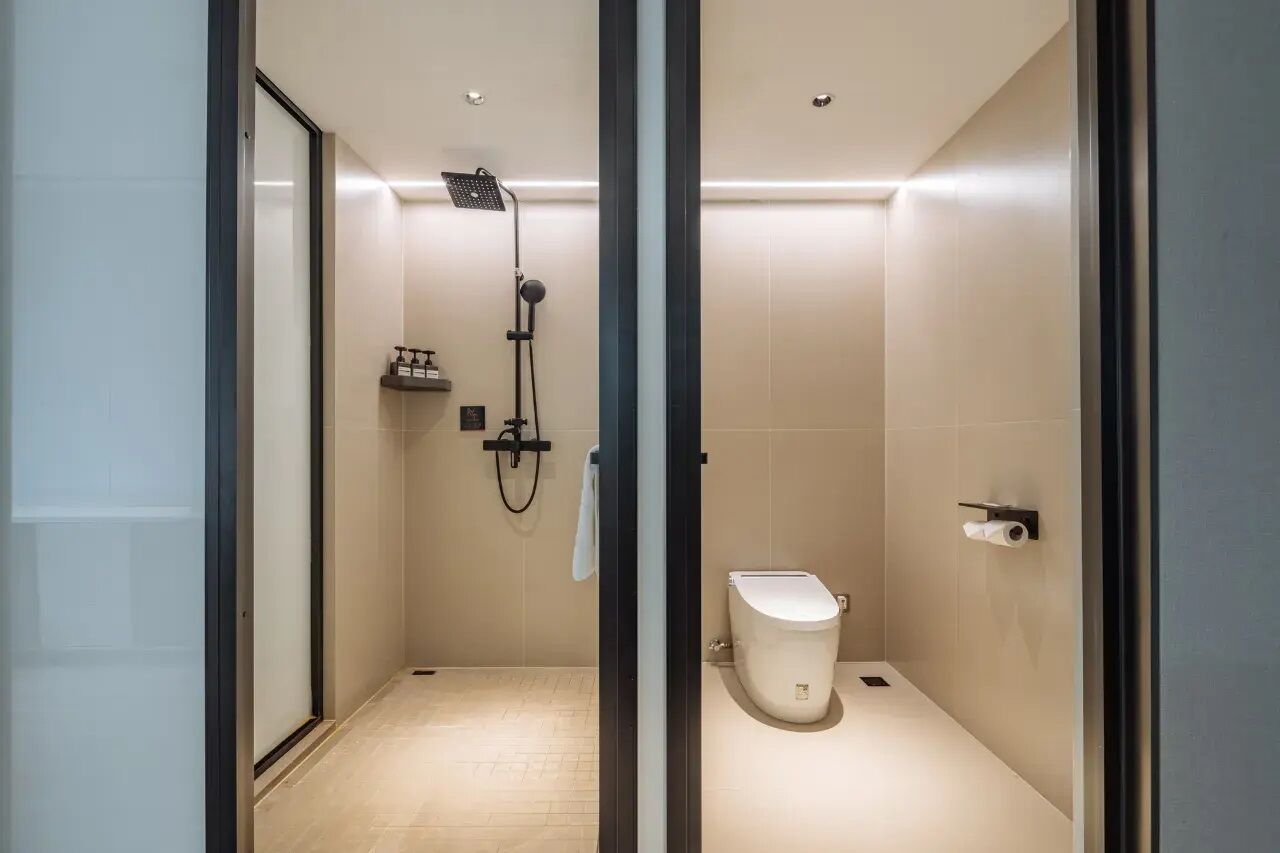 A modern bathroom with a glass-enclosed shower, a toilet, and a shelf with toiletries.