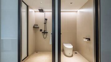 A modern bathroom with a glass-enclosed shower, a toilet, and a shelf with toiletries.