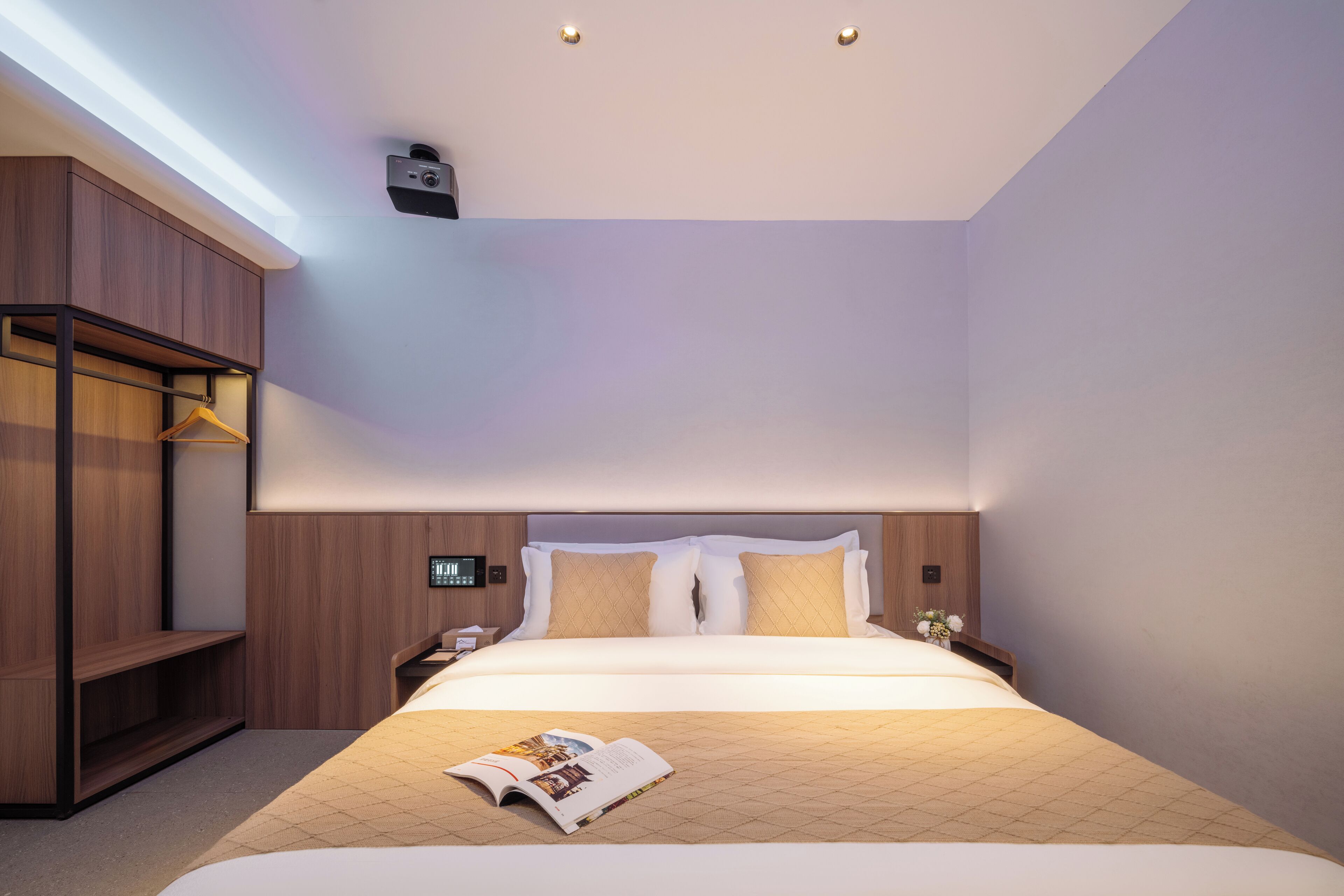 A modern hotel room with a large bed, a wooden wardrobe, a bedside table, and a nightstand.