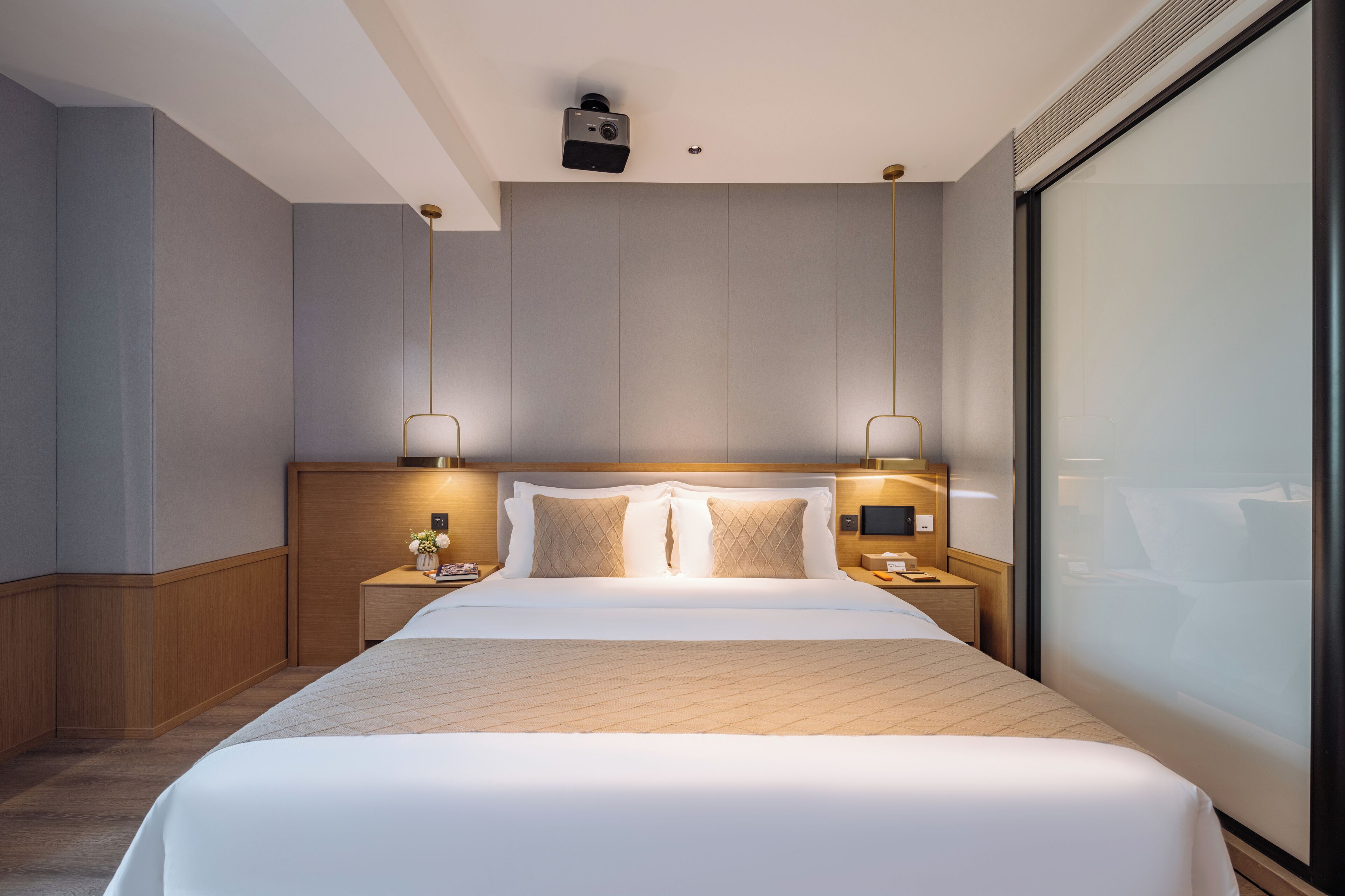 A modern hotel room with a large bed, wooden headboard, two bedside tables with lamps, and a large window.