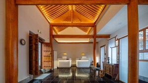 Un hall d’entrée spacieux, doté d’un haut plafond et de poutres en bois, qui mène à un espace d’accueil avec un bureau moderne et des sièges.