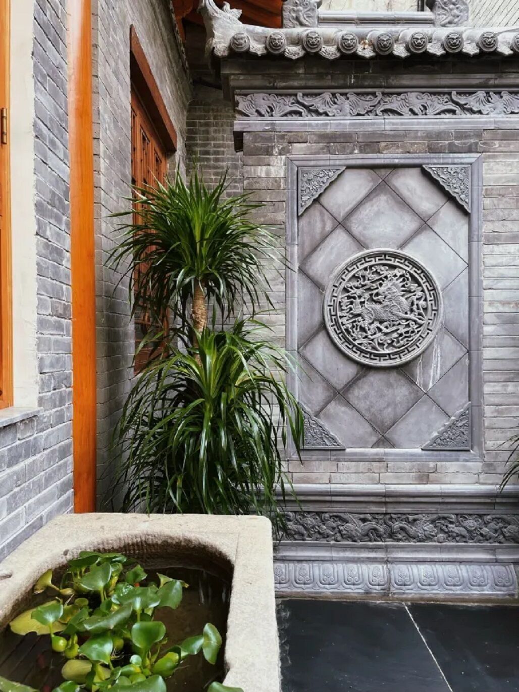 A traditional courtyard with a stone wall, a decorative circular emblem, and a water feature with aquatic plants.