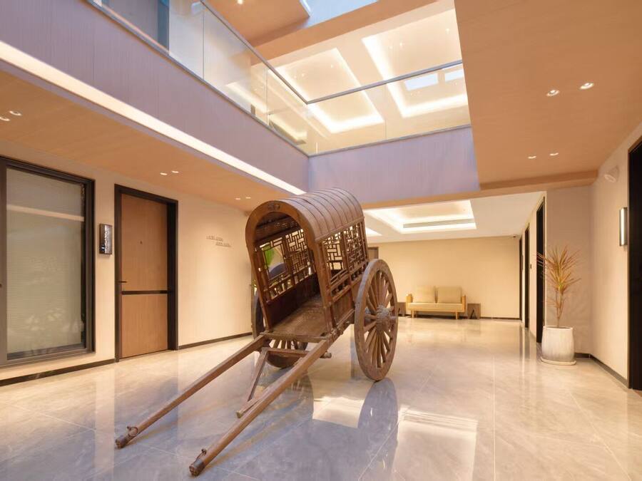 A modern hotel lobby with a wooden carriage in the center, a sofa, and a potted plant.