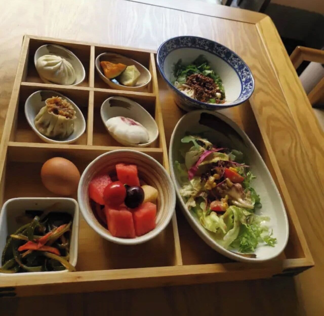 A wooden table with a variety of food items including a bowl of salad, a bowl of fruit, and several small dishes with different foods.