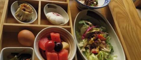 A wooden table with a variety of food items including a bowl of salad, a bowl of fruit, and several small dishes with different foods.