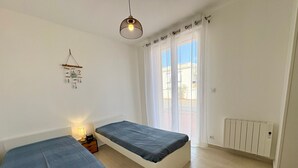 Ett sovrum med två sängar, en hängande lampa, ett element och ett fönster med gardiner.