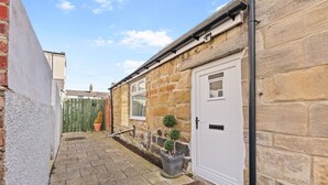 A narrow stone pathway leading to a white door, flanked by a brick wall and a wooden fence.