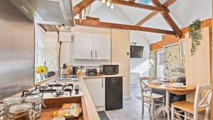 A compact kitchen with a gas stove, microwave, and a small refrigerator. There is a dining area with a wooden table and chairs.