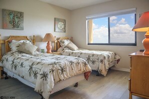 A bedroom with two beds, a window with a view of the sky, and artwork on the walls.