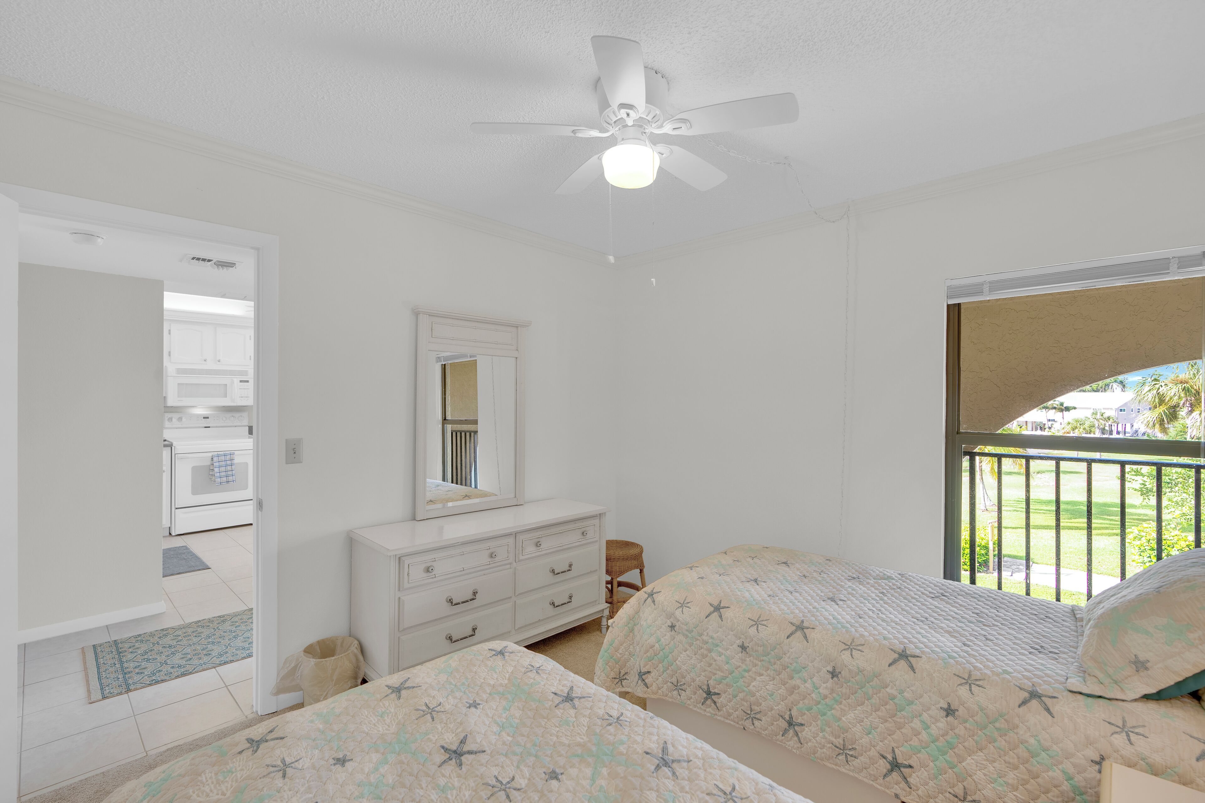 Une chambre avec deux lits, un ventilateur de plafond, une commode et une fenêtre donnant sur l’extérieur.