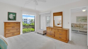 Quarto com cama, cómoda de madeira e ventoinha no teto.
