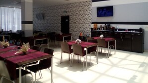Uma área de refeições com mesas e cadeiras, um bar com garrafas, e uma televisão na parede.