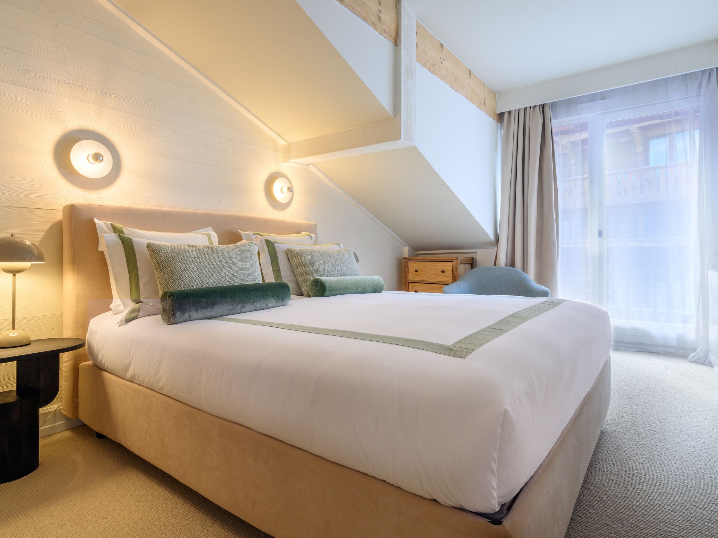 A modern hotel room with a large bed, two bedside tables, a nightstand, and a window with curtains.
