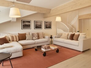 A modern living room with two white sofas, a glass coffee table, and a spiral staircase.