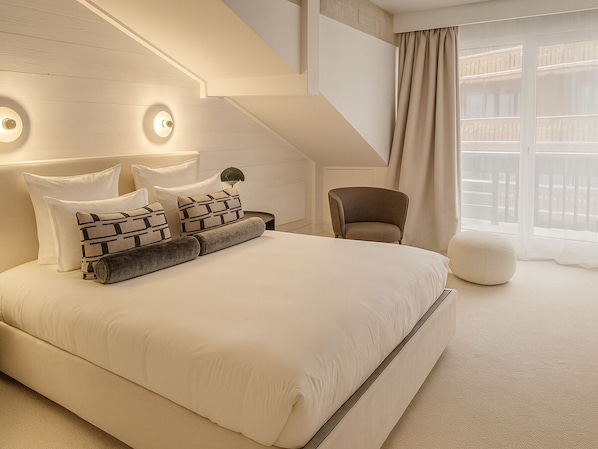 A modern bedroom with a large bed, a chair, and a window with curtains.
