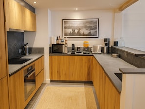 A modern kitchen with wooden cabinets, a microwave, a coffee maker, and a framed landscape painting on the wall.